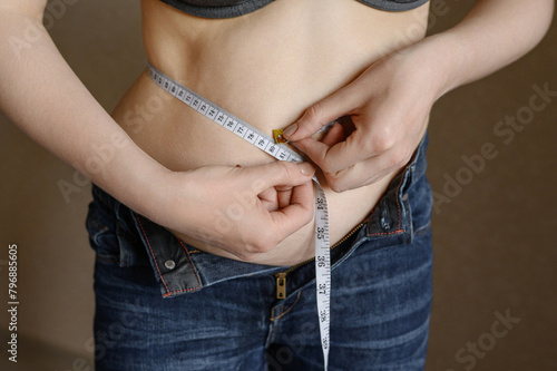 Woman measures her fat belly with a tape measure on a gray background, close-up. Problem of excess weight. Concept of losing weight, getting rid of excess weight, obesity.