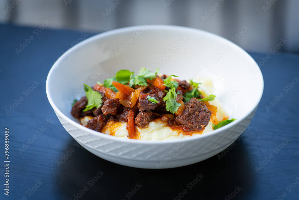 Beef dish with mashed potatoes and skillet fried vegetables (orange bell peppers) with cilantro on top - close up Beef dish with mashed potatoes and skillet fried vegetables (orange bell peppers) with cilantro on top - close up