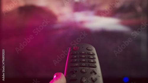 Woman with remote in hand switching channels, smart tv technology internet video content, screen with content at the background close up shot.