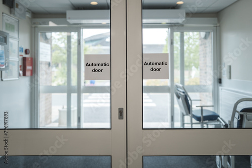 Automatic doors seen at the exit of an NHS outpatients department in a busy British hospital. Porters wheelchairs can be seen in the lobby area for immobile outpatients.