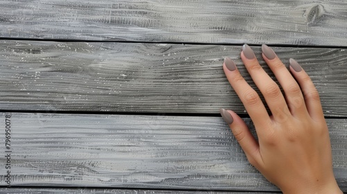 Close-up of a woman's hand with taupe nail polish on a weathered wooden background. Nail fashion and beauty concept for design and print