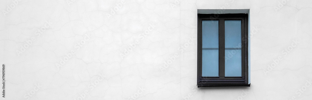 White wall of the house with a small window. Lonely window on the white wall of the building. View of a fragment of a wall with one window. Lonely window on the white wall of the house.