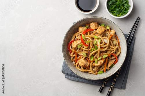 Stir fried udon noodles with chicken and vegetables in bowl on concrete background