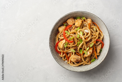 Stir fried udon noodles with chicken and vegetables in bowl on concrete background