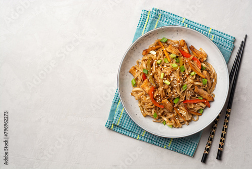 Stir fried udon noodles with chicken and vegetables in plate on concrete background