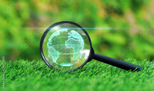 Magnifying glass focused on digital earth globe on the grass in green garden background. Business cooperation for a sustainable environment.ESG environment social governance concept.