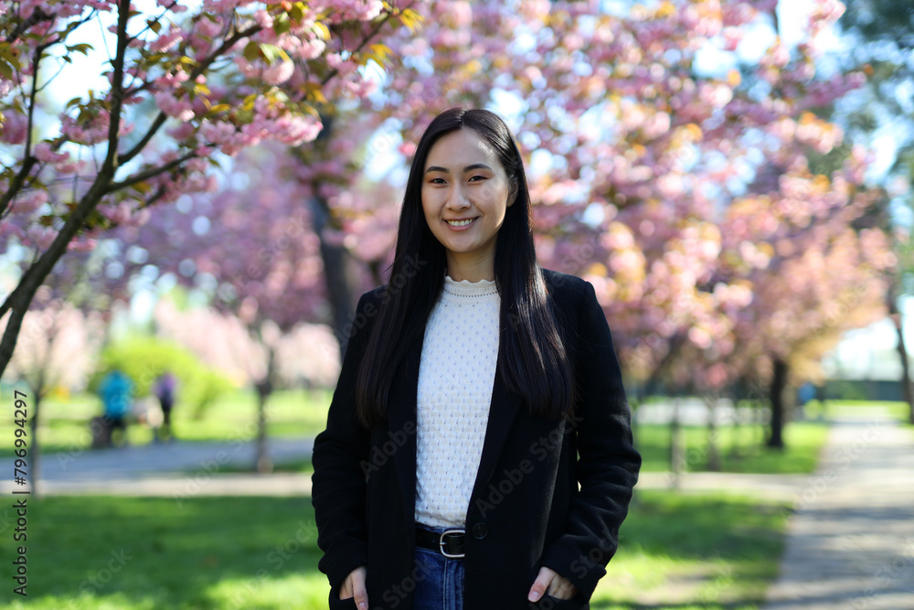 A successful professional Korean woman, happy and confident, smiles in the sunlight against a nature background. A successful professional Korean woman, happy and confident, smiles in the sunlight against a nature background.