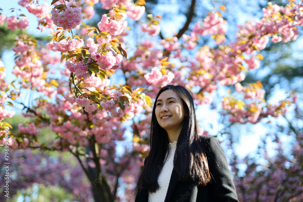 In a Japanese springtime garden, a young woman poses under blooming sakura, radiating beauty and happiness. In a Japanese springtime garden, a young woman poses under blooming sakura, radiating beauty and happiness.