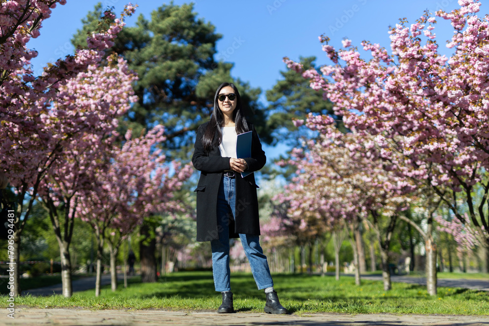 A Japanese woman strolls through a park lined with blooming sakura trees in the warm springtime. A Japanese woman strolls through a park lined with blooming sakura trees in the warm springtime.