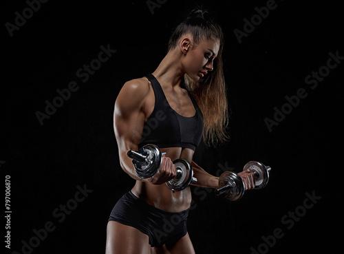 Sporty brunette woman in sports underwear posing in studio with dumbbells