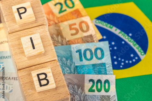The word PIB (Gross Domestic Product) written on wooden cubes with Brazilian real money in yellow, green flag of Brazil. Brazilian Portuguese language