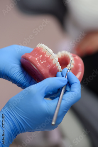 Female hands of an orthodontist in rubber gloves close-up. A dentist demonstrates artificial human jaws with dental braces for teeth correction. The patient visits the doctor for orthodontic issues.