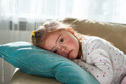Portrait of cute little girl with Down syndrome looking at camera lying down on pillow photo