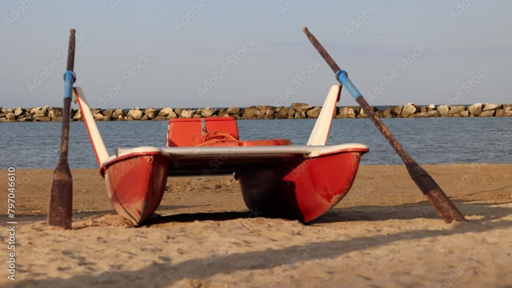 Classic italian rescue boat flanked by oars or rescue rowing catamaran on the sandy beach on the sunset symbolizing preparedness and safety along shoreline.Vacation concept. Classic italian rescue boat flanked by oars or rescue rowing catamaran on the sandy beach on the sunset symbolizing preparedness and safety along shoreline.Vacation concept.