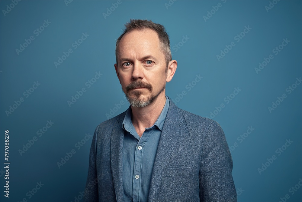 A man in a blue jacket and blue shirt is standing in front of a blue wall A man in a blue jacket and blue shirt is standing in front of a blue wall