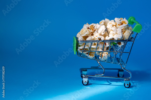 Freshly made popcorn in a shopping cart on a blue background