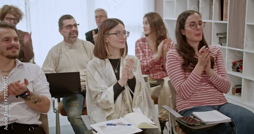 A group of smiling businesspeople in a modern office classroom is applauding during a professional training or seminar, demonstrating their appreciation for the valuable insights shared.