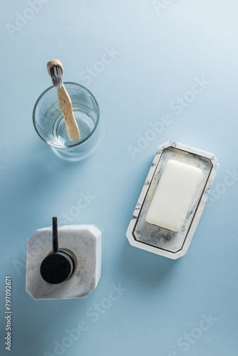 Set of cosmetics and bathroom accessories seen from above, on a glass table and a blue marble background.