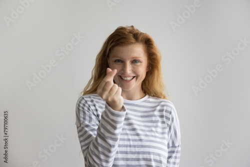 Portrait of attractive ginger woman showing cash gesture, rubbing their fingers, staring at camera posing on gray studio background. Wealth, abundance, financial matters, business idea to earn income