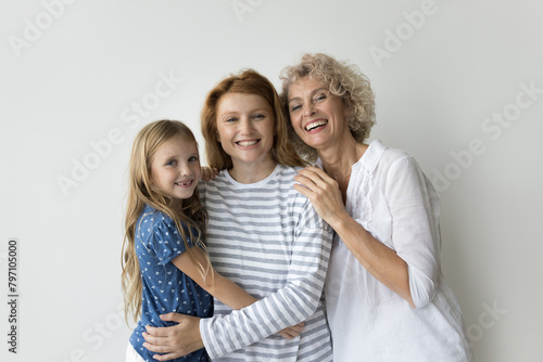 Beautiful multi-generational relative women hugging posing on gray studio background, smile look at camera enjoy their harmonic relationship, friendship and family ties, showing togetherness and unity © fizkes