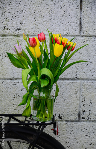 A bouquet of tulips in a glass jar on the trunk of a bicycle.