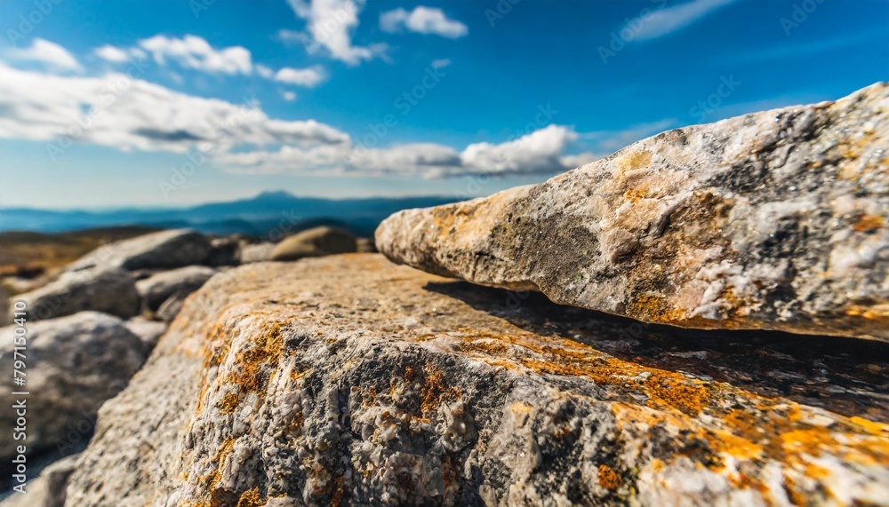 a horizontal low perspective rock for a product display showing close detail to the rear edge of the stone surface with a blurred cloud and boulder background