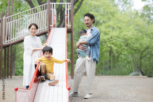 新緑の公園の滑り台で遊ぶアジア人（日本人）の親子 4人家族 子育てや育児の休日のイメージ