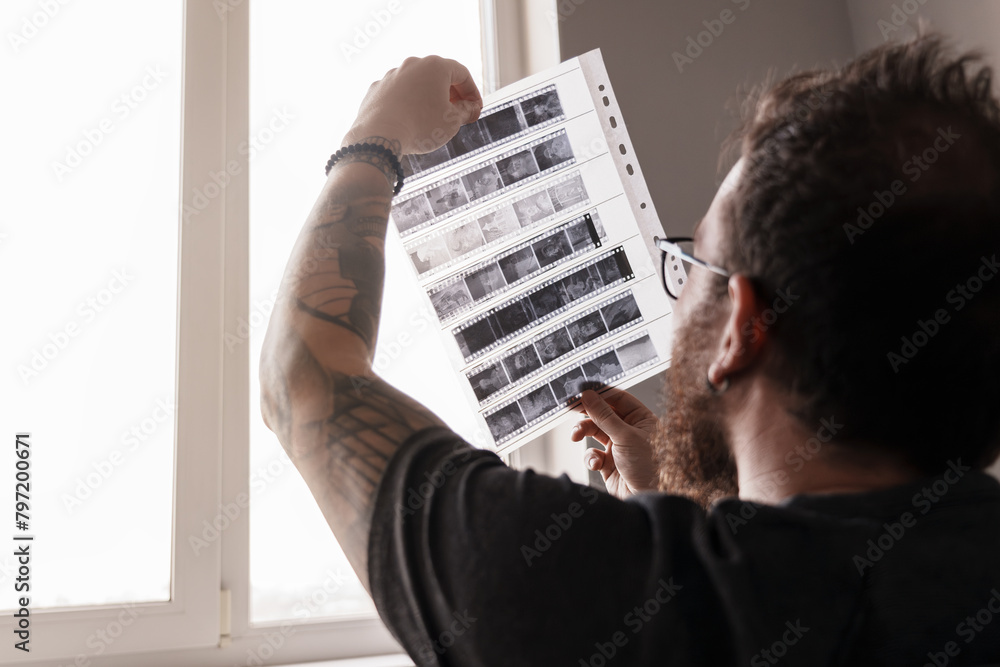 Naklejka premium Close-up of a bearded photographer holding and inspecting film negatives in natural light by a window.