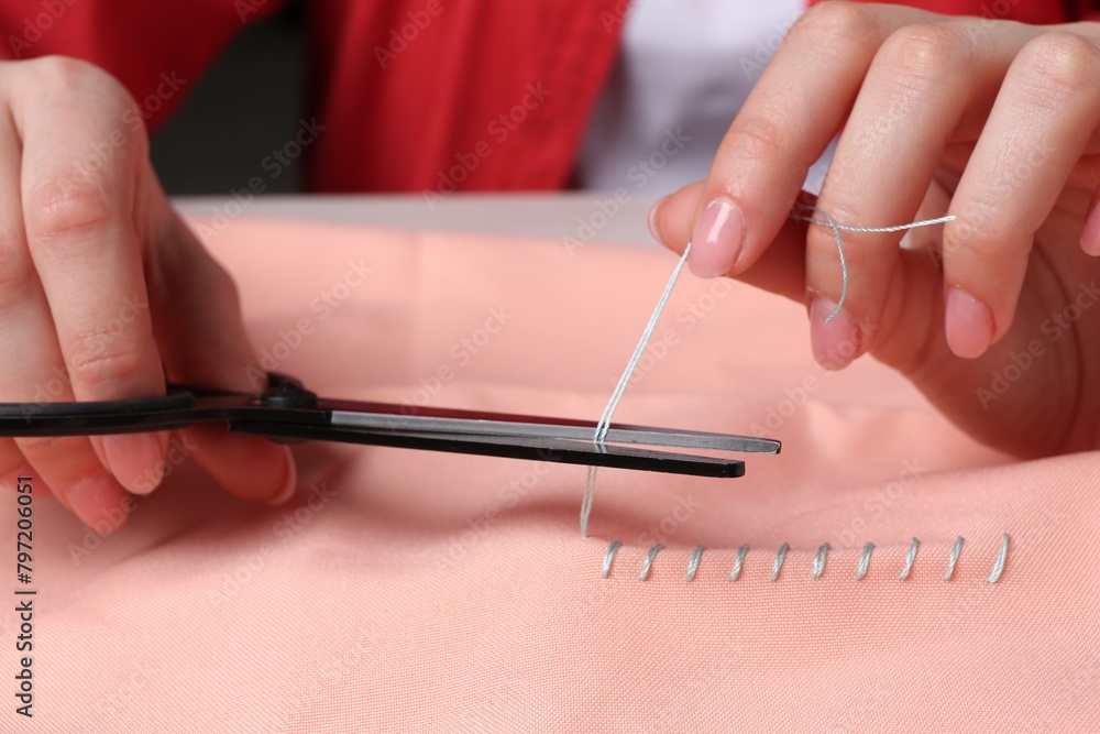 Woman cutting sewing thread over cloth, closeup Woman cutting sewing thread over cloth, closeup