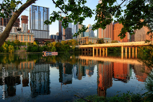 Golden hour in Austin, Texas. The cityscape reflected on the surface of Lady Bird Lake, accompanied by the gliding of a river boat tour. Perspective from the waterfront's edge during a summer evening. photo