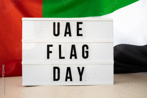Lightbox with text UAE FLAG DAY on United Arab Emirates waving flag made from silk material. Independence Commemoration Day Muslim Public holiday celebration background. The National Flag of UAE
