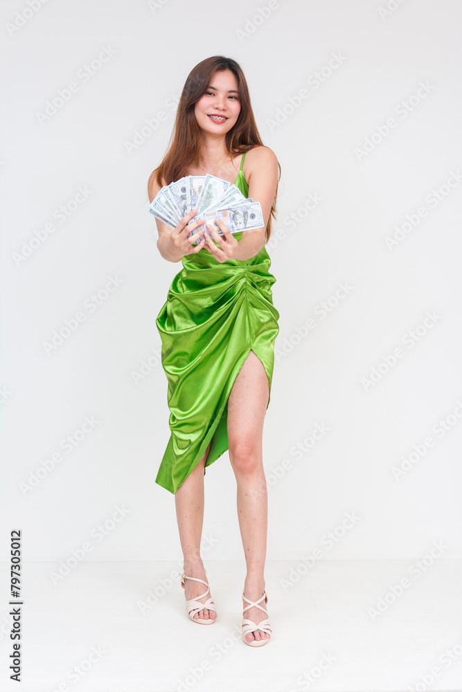 Full body photo of an attractive young woman in a light green silk dress, seductively holding a fan of dollar bills, isolated on a white background. Concept of wealth and temptation. Full body photo of an attractive young woman in a light green silk dress, seductively holding a fan of dollar bills, isolated on a white background. Concept of wealth and temptation.