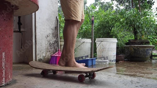 Slowmotion footage of a man washing his feet with a thin stream of water from a pipe. A skateboard sits unmoving in the foreground, amidst the calm of the house yard photo