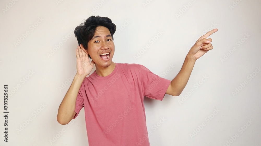 Excited young handsome Asian man happy, cheerful and enthusiastic posing pointing to his side and posing as if listening with an isolated white background Excited young handsome Asian man happy, cheerful and enthusiastic posing pointing to his side and posing as if listening with an isolated white background