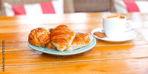 Croissant banner on a blue plate on a wooden table next to coffee. Delicious fresh pastries and desserts for breakfast.