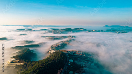a breathtaking view of Dalat City enveloped in mist, with mountains, forests, and buildings peeking through the serene clouds under the soft morning light.