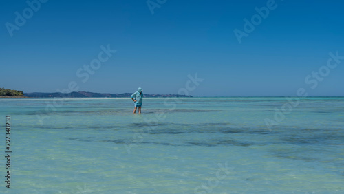 The man is standing knee-deep in water. The endless aquamarine ocean stretches to the horizon. Islands in the distance. Clear blue sky. Copy space. Madagascar. Nosy Iranja