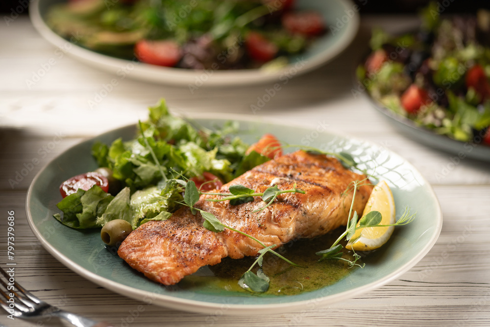 Grilled fried salmon steak with vegetables in white plate on wooden table.