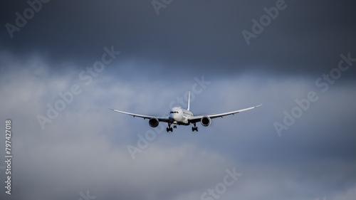 A large passenger airplane coming in for a landing at the airport, with storm clouds in the background.