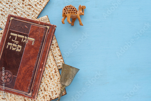 Matzah, decorative camel, Kiddush cup, book with text in Hebrew: "Passover Haggada" ("Passover Tale") on blue wooden background. Jewish holiday Pesach background..