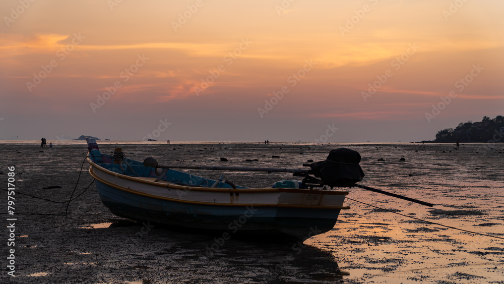 Boat grounded on beach as sunset on the horizon, casting a warm afterglow Boat grounded on beach as sunset on the horizon, casting a warm afterglow