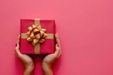 Male and female hands holding red gift box on pink background.