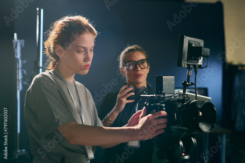 Side view portrait of female cameraman operating equipment on set with assistant in background copy space