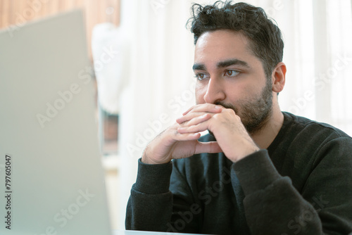 Serious pensive businessman in shirt thinking about decision sitting at table in modern office, man with beard is using laptop at work.
