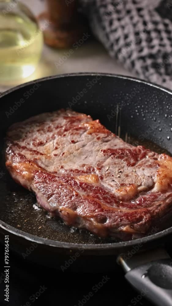 Chef sprinkles pepper on beef steak frying on pan in kitchen, close-up Chef sprinkles pepper on beef steak frying on pan in kitchen, close-up