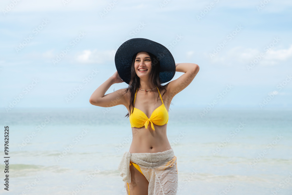 Woman in a bikini relishing her time on a tropical beach. She relaxes on the sandy shore, embodying the essence of summer vacation.