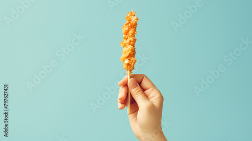 Hand holding a fried chicken stick on blue background photo