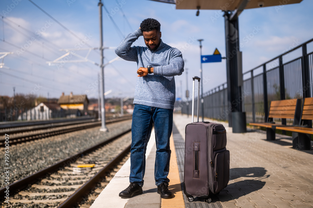 Worried man looking at his clock while standing with suitcase on a railway station. Worried man looking at his clock while standing with suitcase on a railway station.