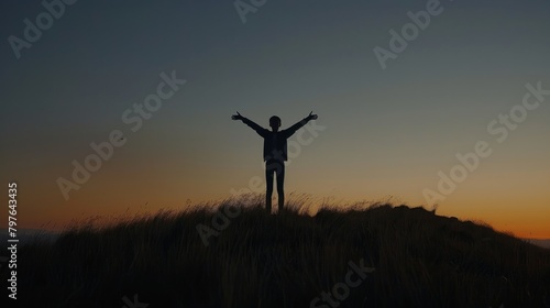 A young person standing on top of a hill during sunset