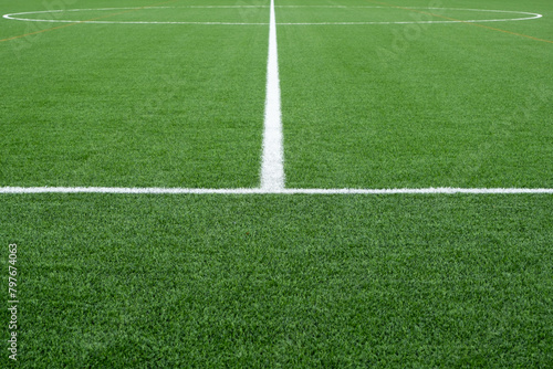Close-up of a soccer field with green, well-maintained artificial synthetic grass painted with thick white lines. Background texture of fake lawn on sports ground. 